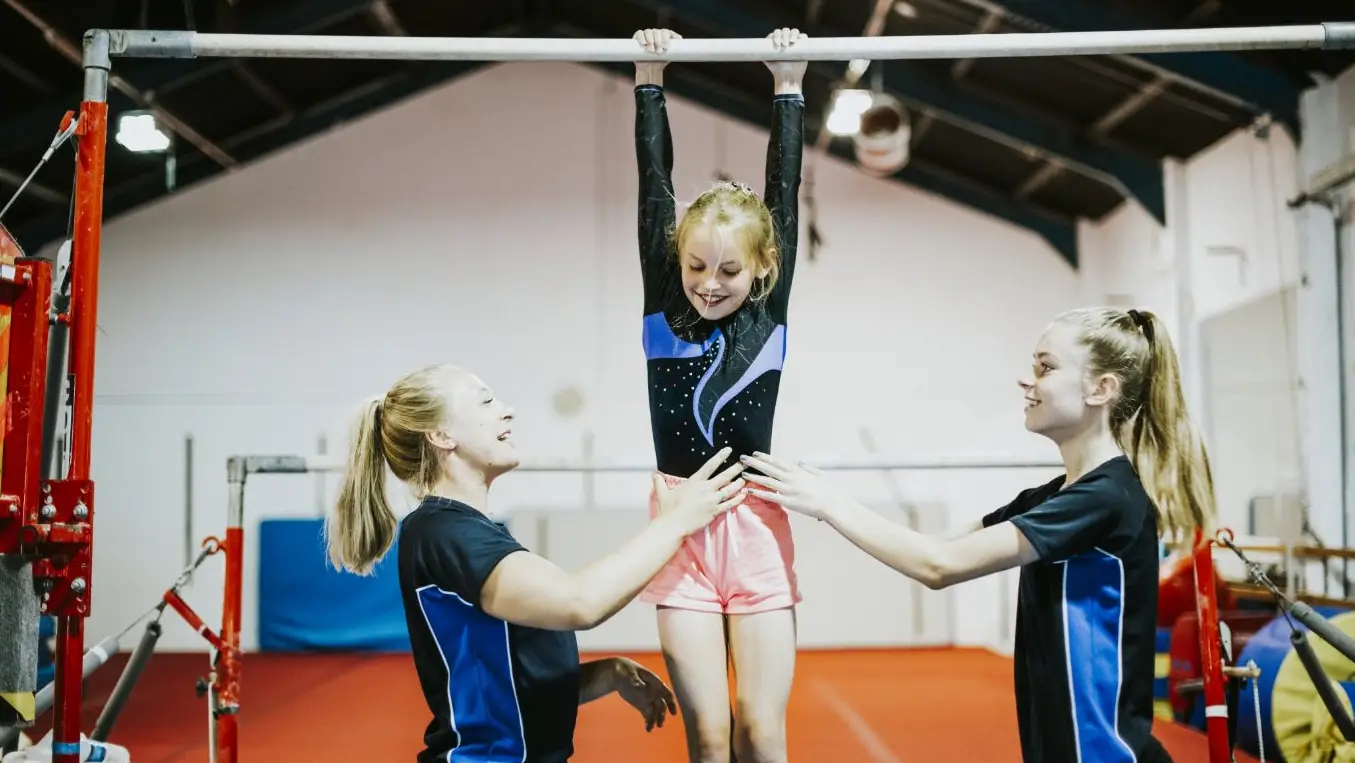 Girl doing gymnastics with two Shine coaches